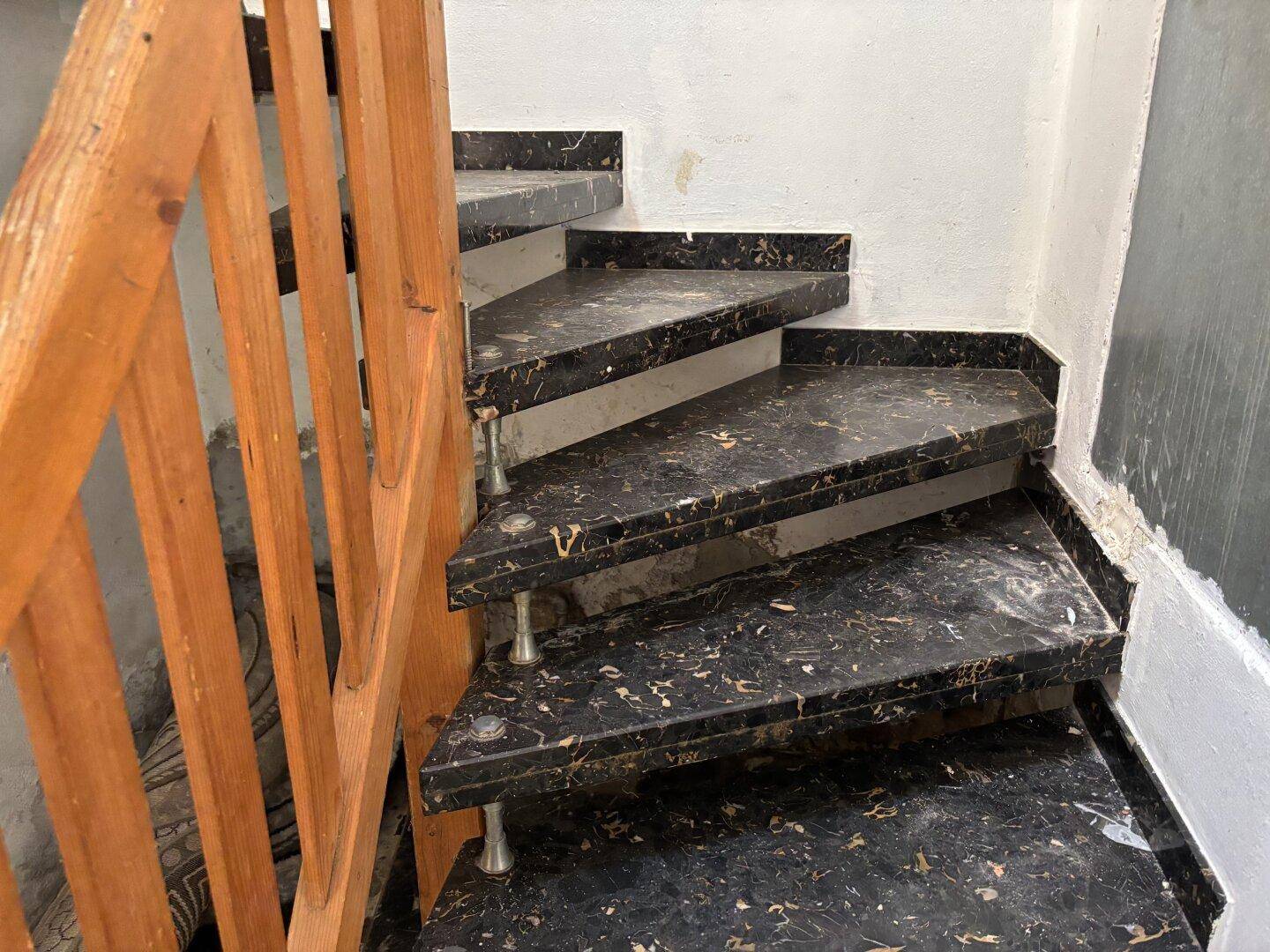 Treppe mit dunklen Marmorstufen und einem Holzgeländer, das renovierungsbedürftig ist.