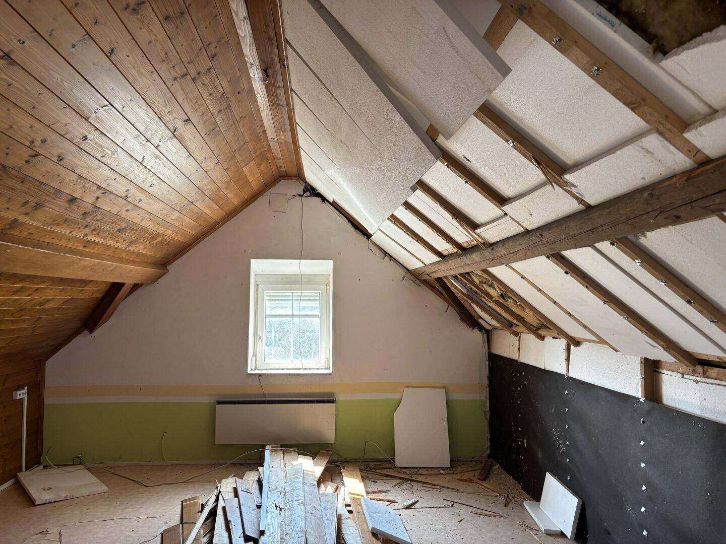 Dachbodenraum in Renovierung mit Holzbalken, Dachschrägen und einem Fenster.