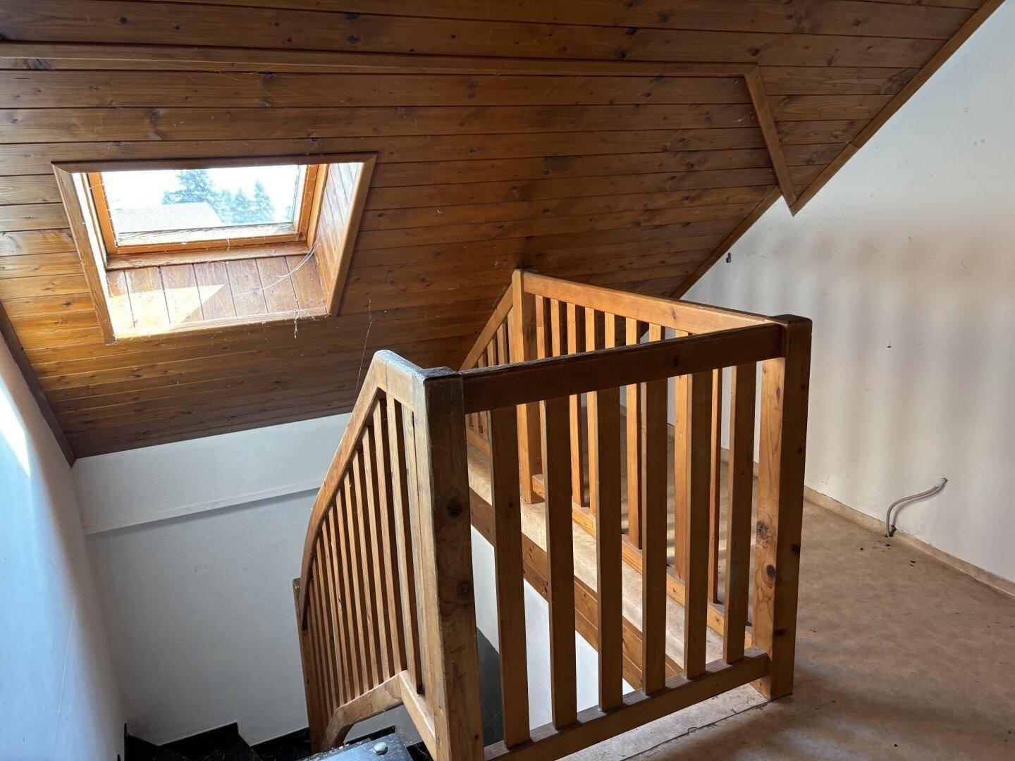 Holztreppe mit Geländer und einem Dachfenster, das natürliches Licht spendet.