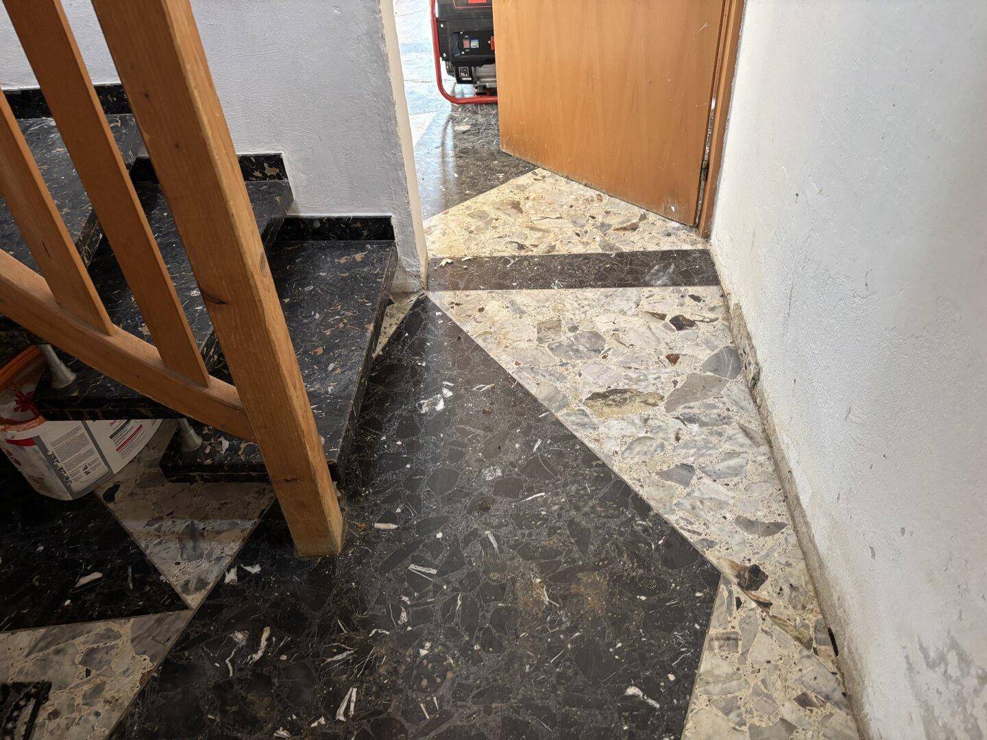 Fliesenboden mit geometrischem Muster in Schwarz und Weiß, neben einer Holztreppe.