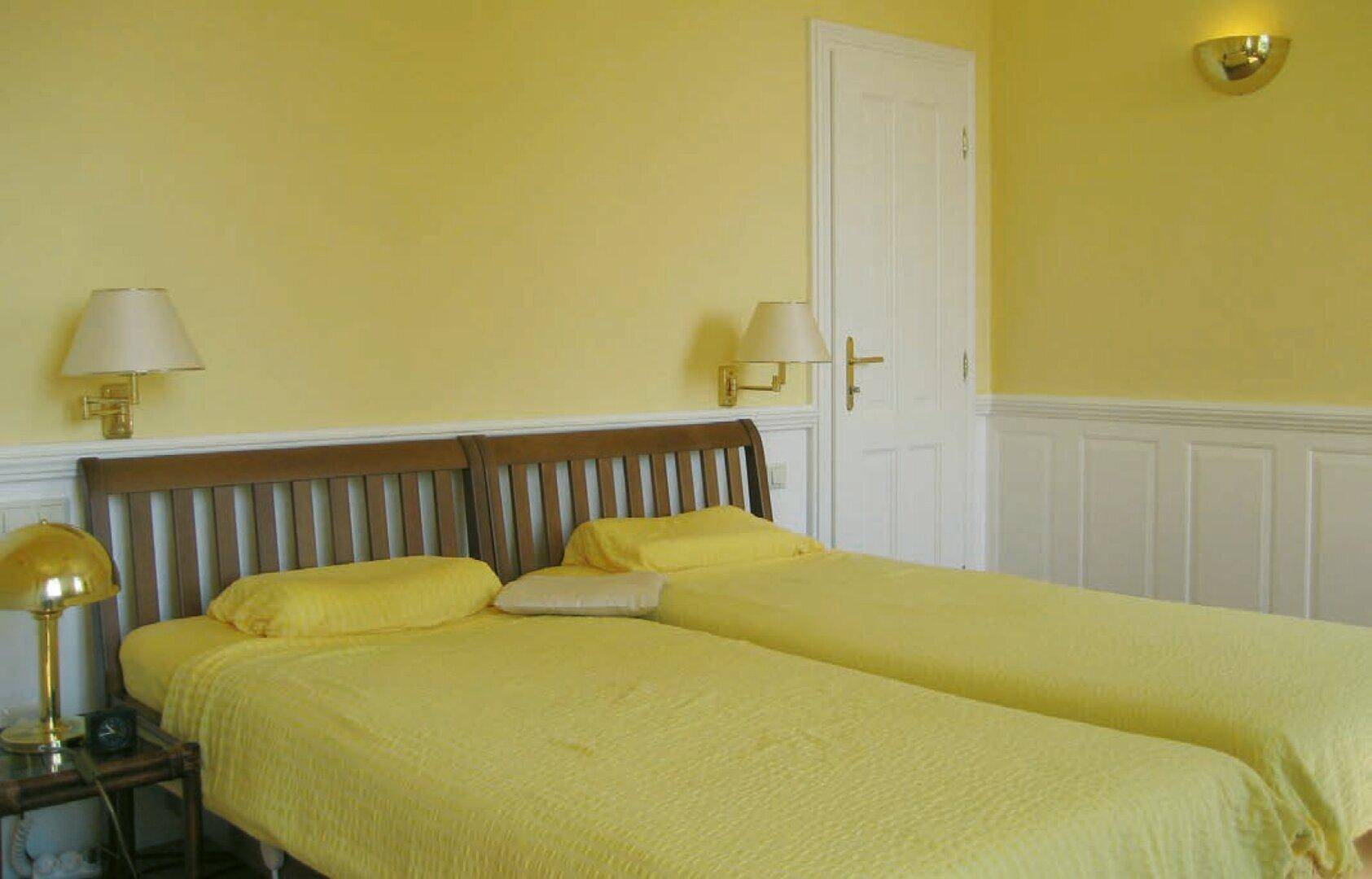 Helles Schlafzimmer mit zwei Einzelbetten, gelben Wänden und Holzvertäfelung.