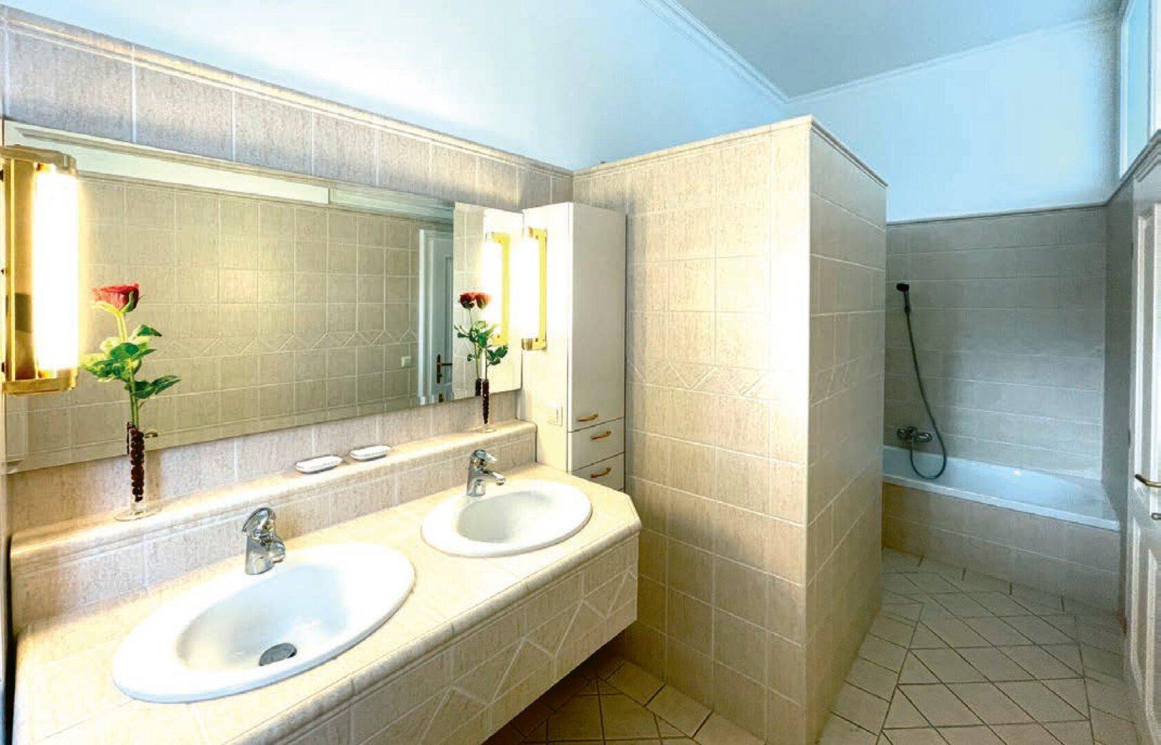 Geräumiges Badezimmer mit Doppelwaschbecken, Badewanne und beigefarbenen Fliesen.