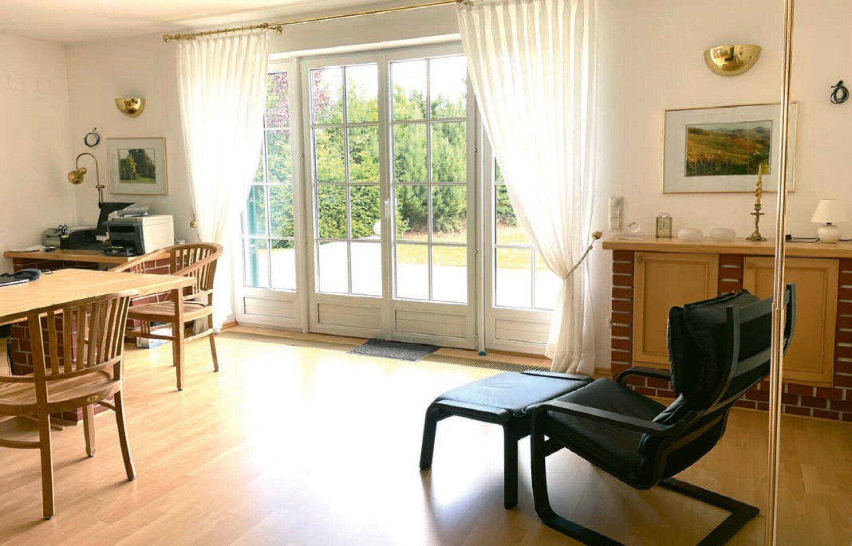 Helles Arbeitszimmer mit Holzboden und direktem Zugang zum Garten durch große Türen.