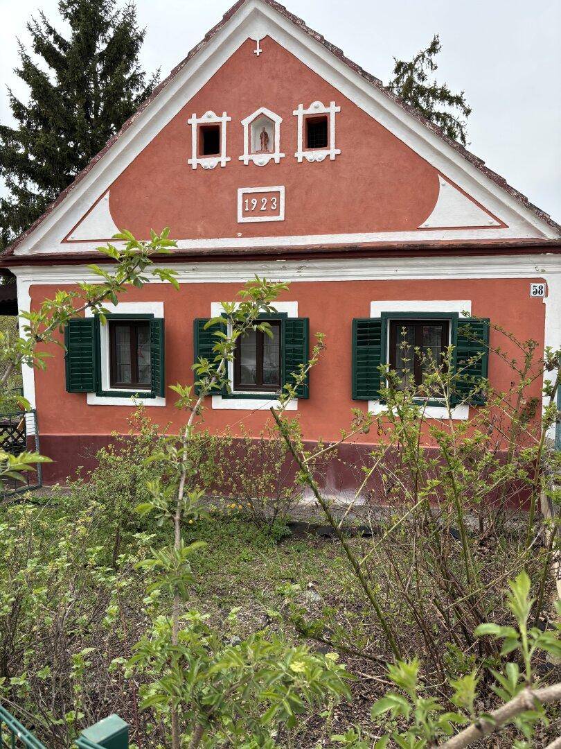 Vorderansicht des historischen Hauses mit markanter roter Fassade und grünen Fensterläden.
