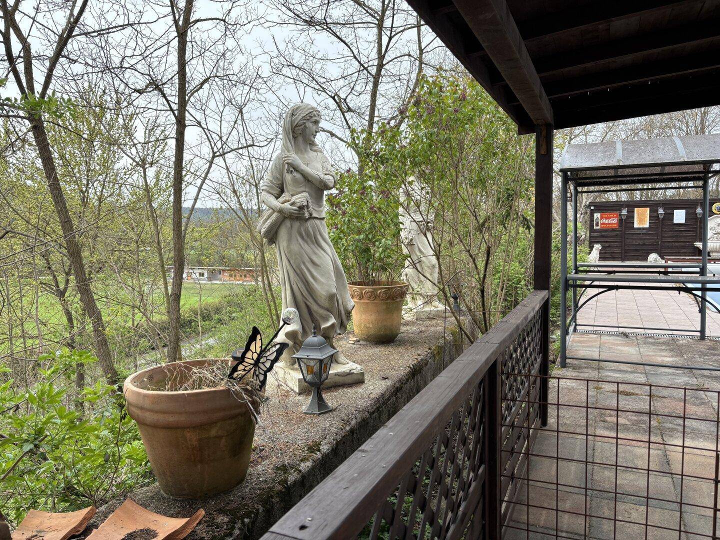 Gartenbereich mit klassischer Statue, Topfpflanzen und Blick ins Grüne.