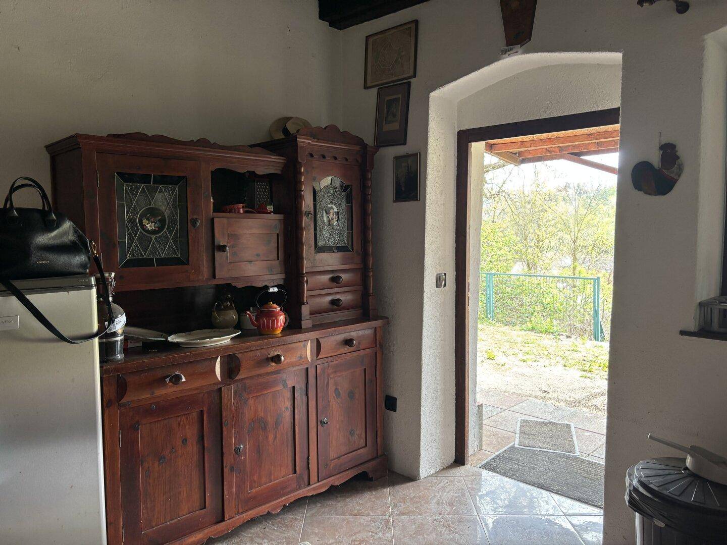 Einfache Küche mit Holzschrank, Kühlschrank und Zugang zum Außenbereich.