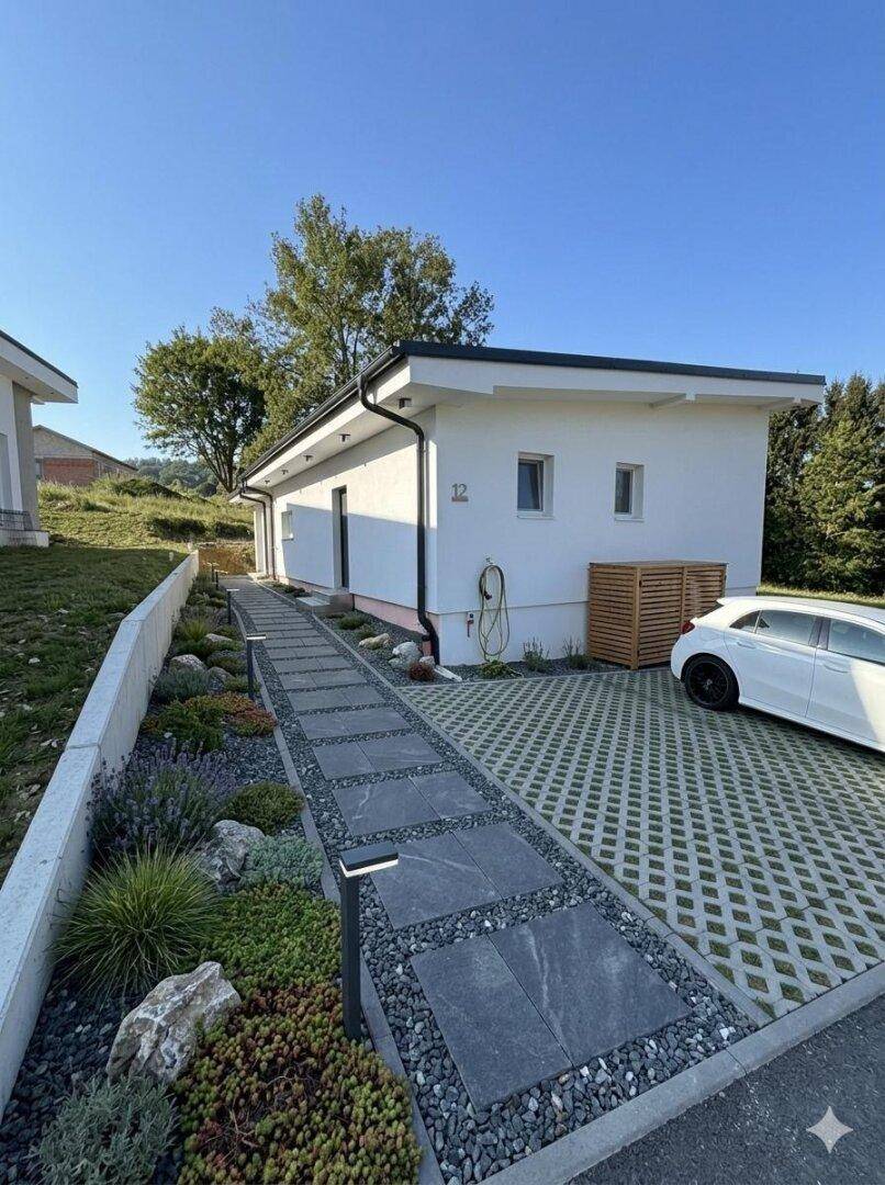 Moderner Vorgarten mit gepflastertem Weg, Bepflanzung und Parkplatz.