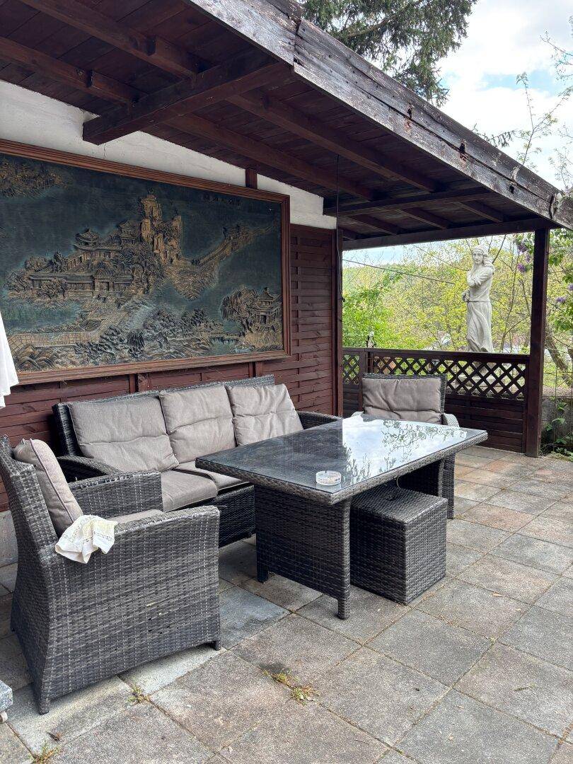 Gemütliche überdachte Terrasse mit Rattanmöbeln und einem großen Wandbild, ideal zum Entspannen.