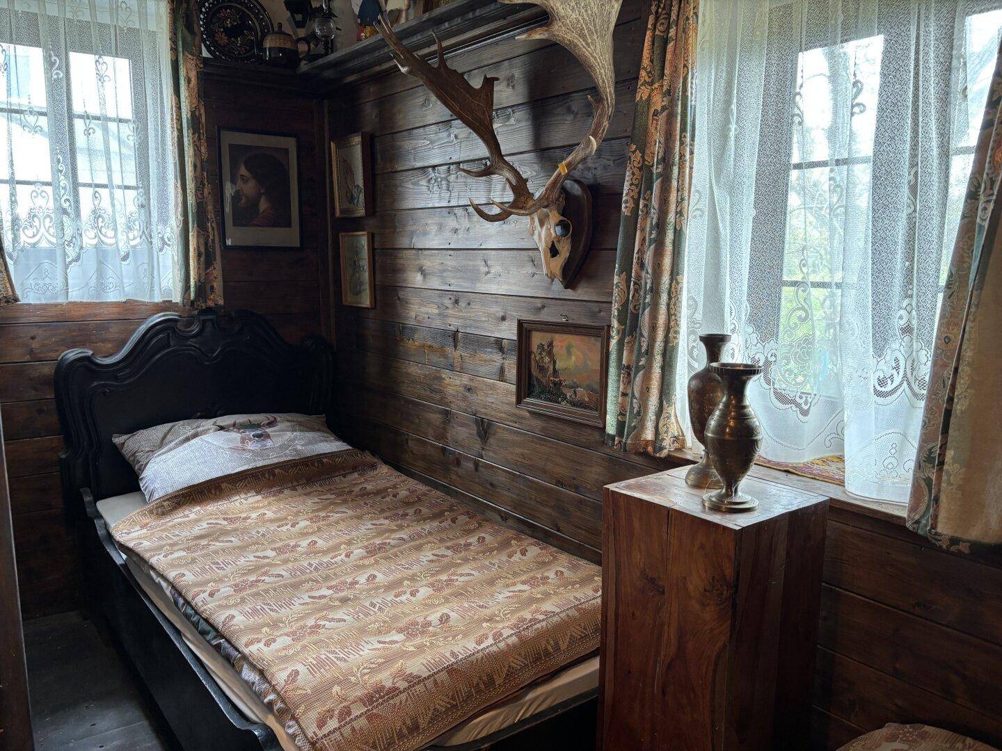 Rustikales Schlafzimmer mit Holzwänden, einem Einzelbett und traditioneller Hirschgeweih-Dekoration.
