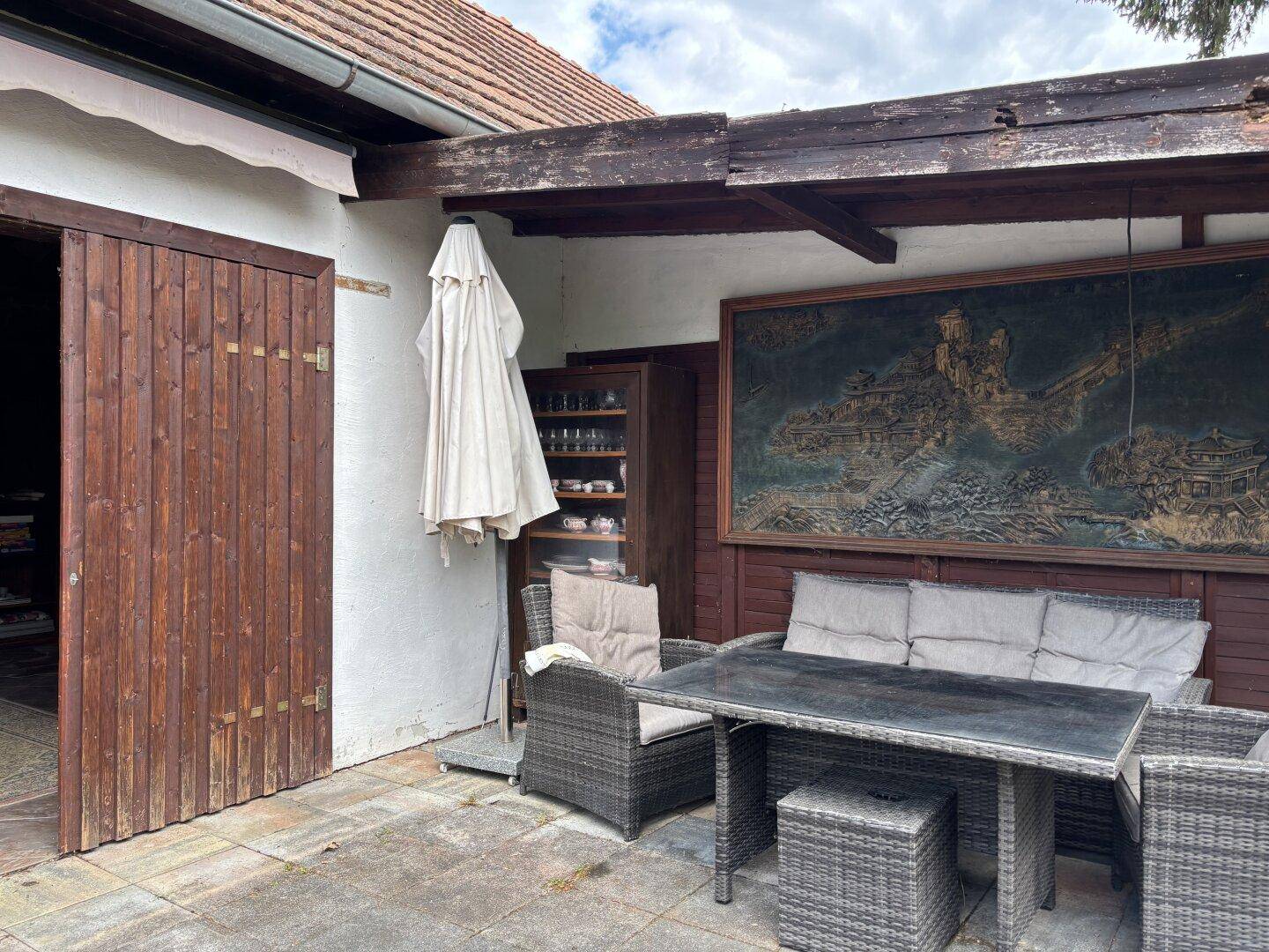 Gepflasterte Terrasse mit Rattanmöbeln und einem großen Wandbild, angrenzend an ein Nebengebäude.
