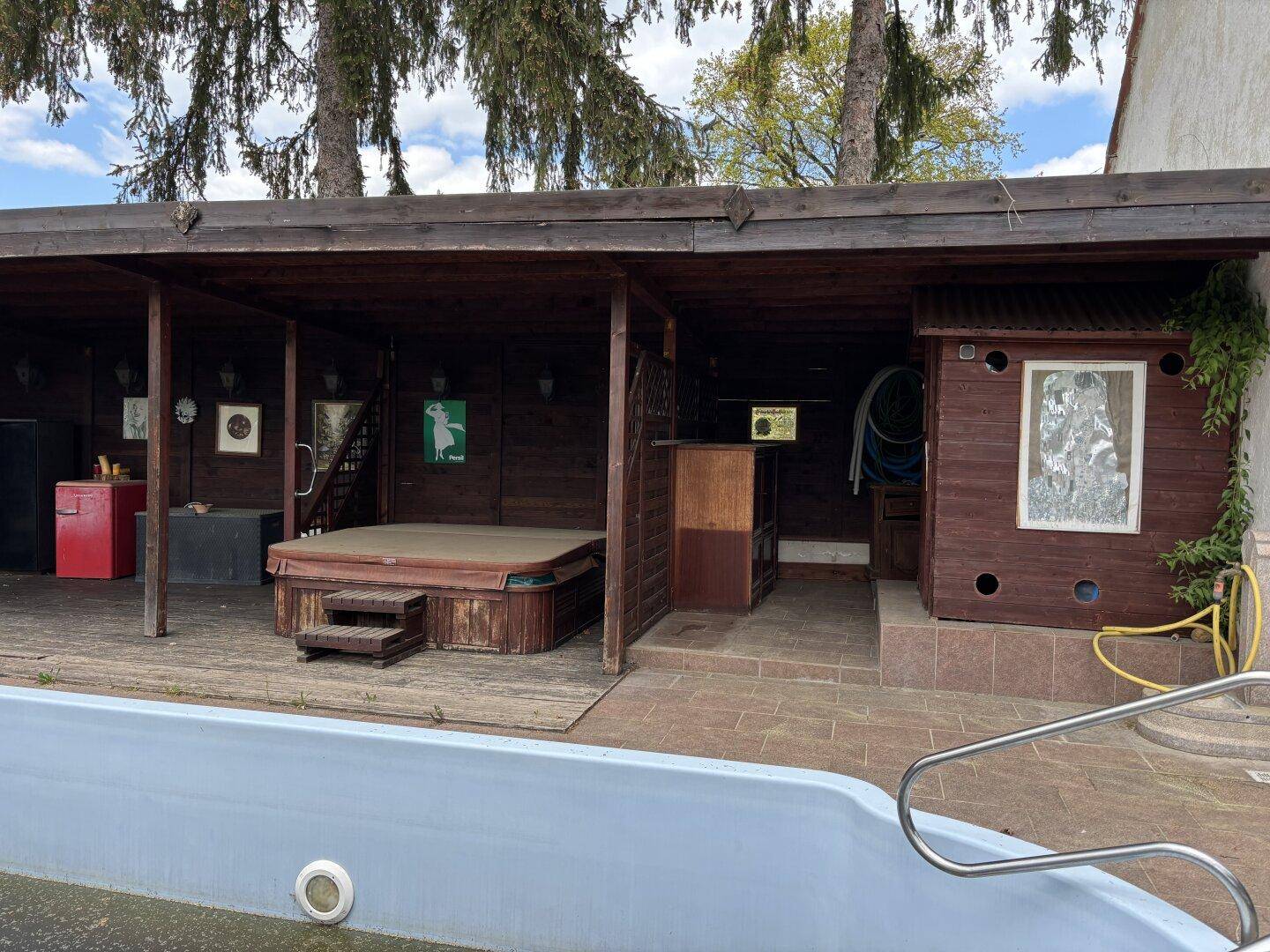 Außenbereich mit Pool und überdachtem Bereich, der einen Whirlpool und eine kleine Hütte beinhaltet.