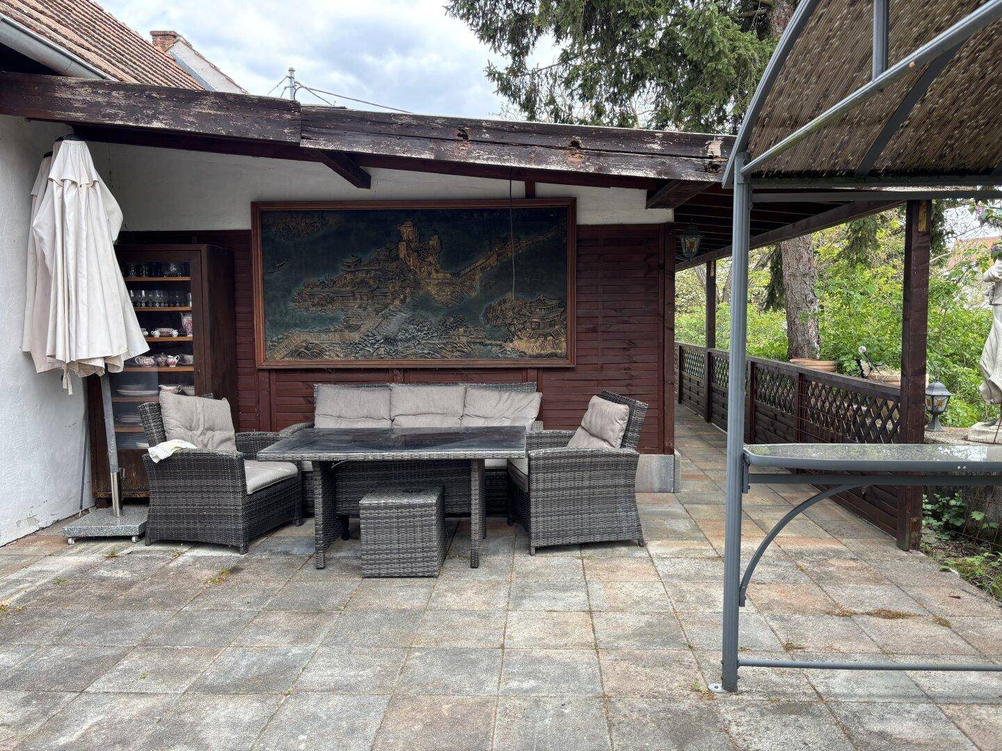 Weitläufige gepflasterte Terrasse mit Rattanmöbeln und einem überdachten Bereich für Mahlzeiten im Freien.