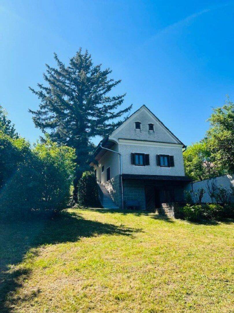 Charmantes Landhaus mit Satteldach und weitläufigem Garten unter strahlend blauem Himmel.
