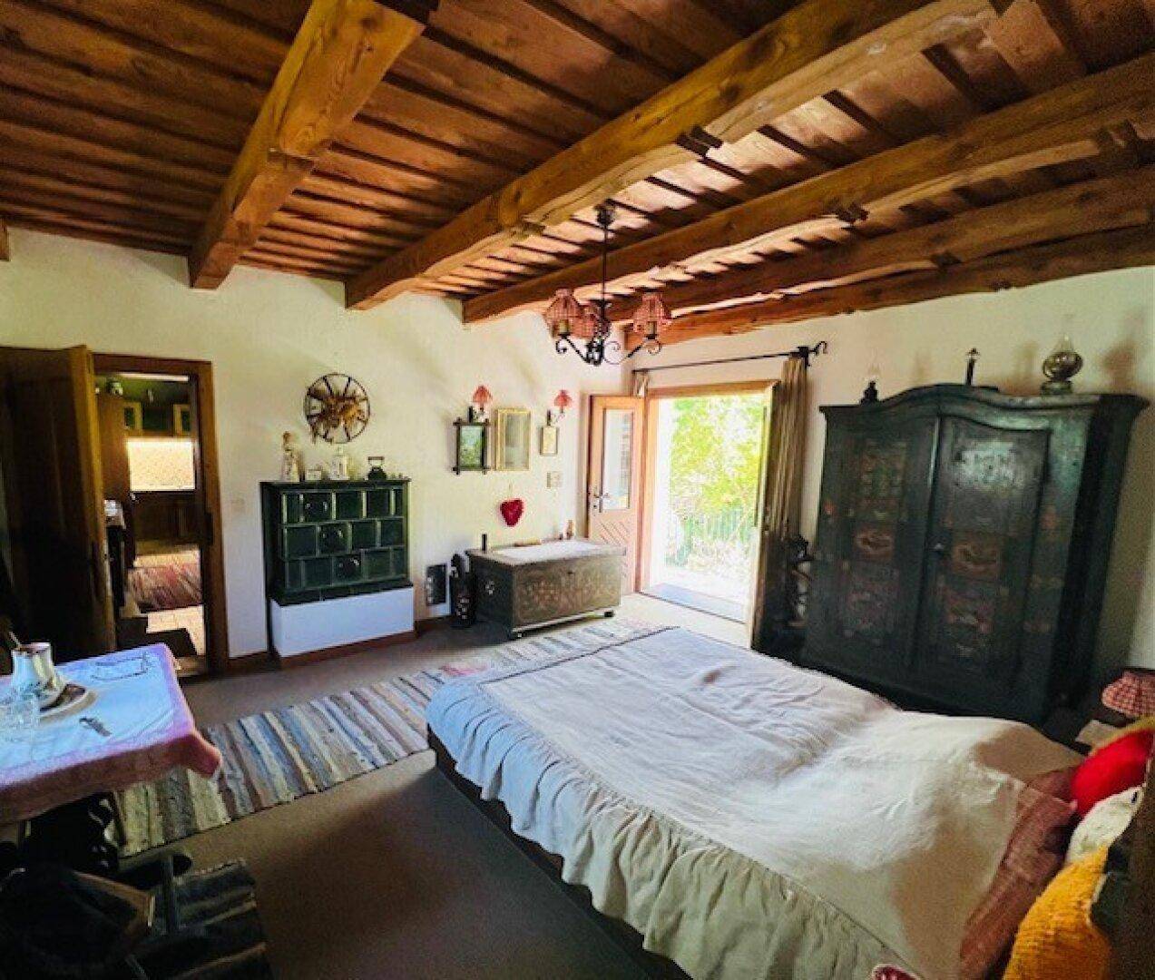 Geräumiges Schlafzimmer mit Holzbalkendecke, Kachelofen und traditionellen Möbeln.