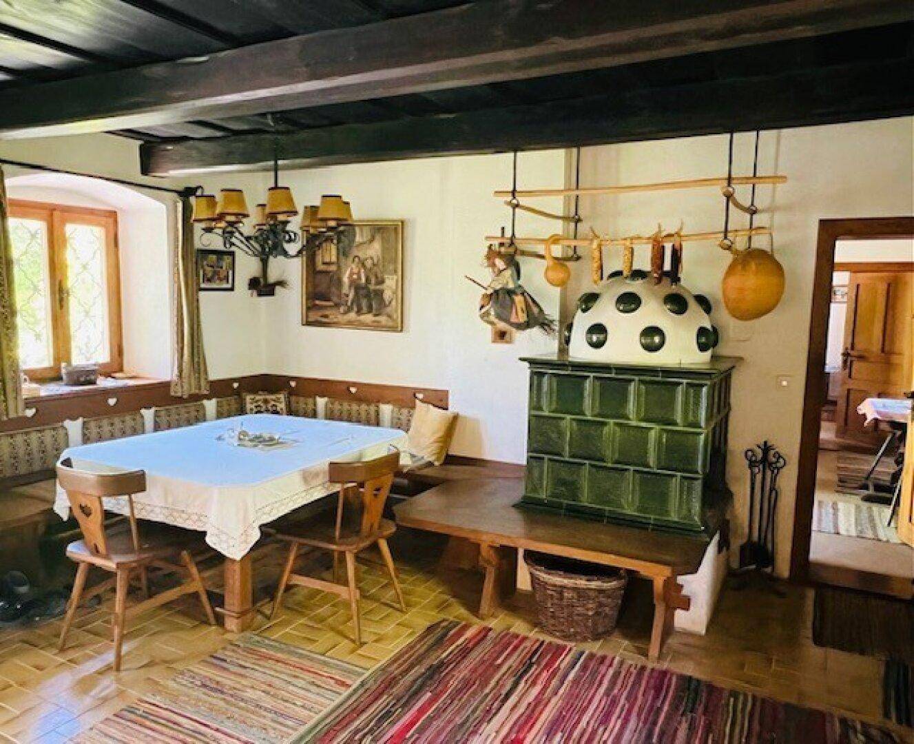 Gemütlicher Essbereich mit Kachelofen, Holzbalkendecke und traditionellen Holzmöbeln.