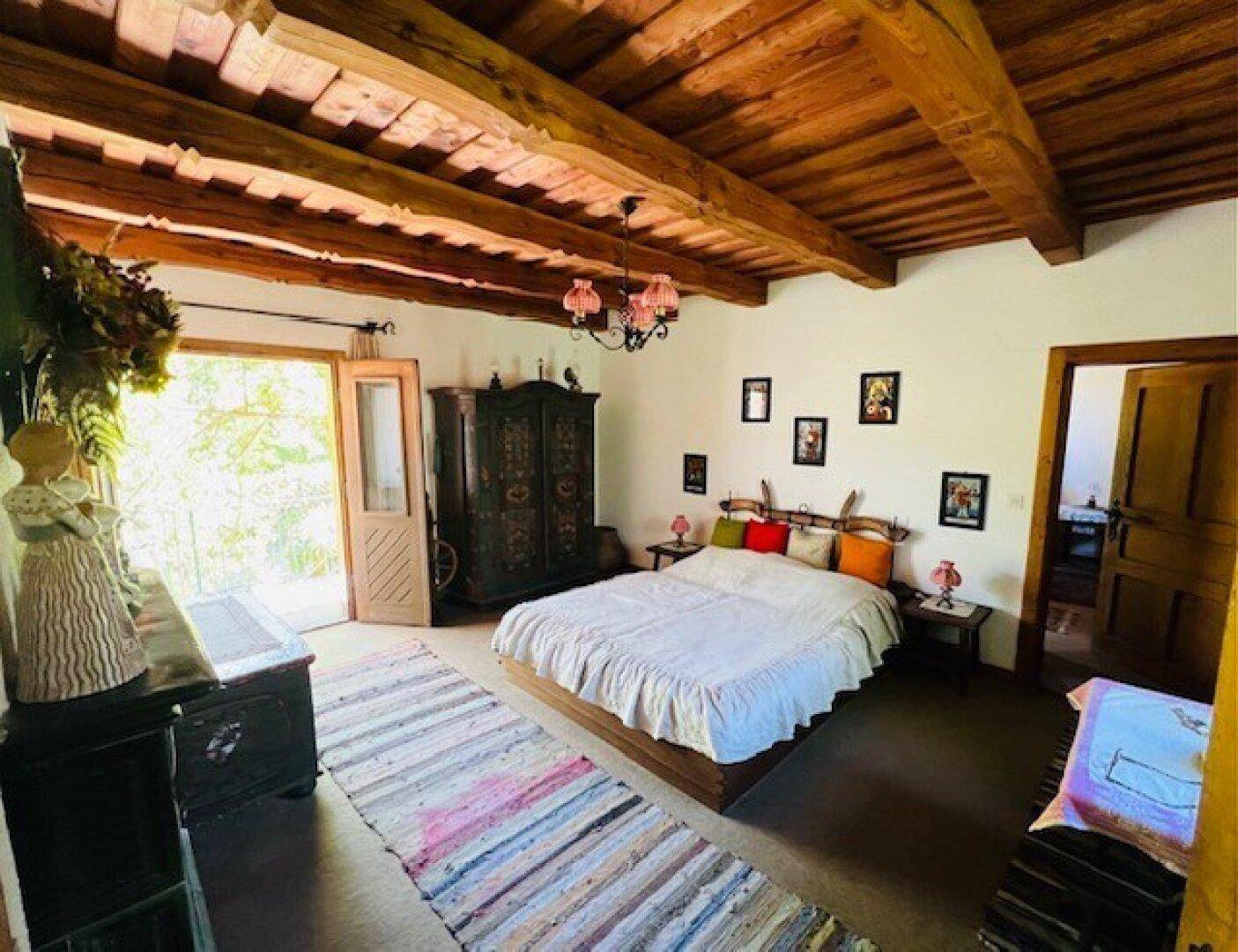 Schlafzimmer mit Holzbalkendecke, traditionellem Bett und Zugang zum Außenbereich.