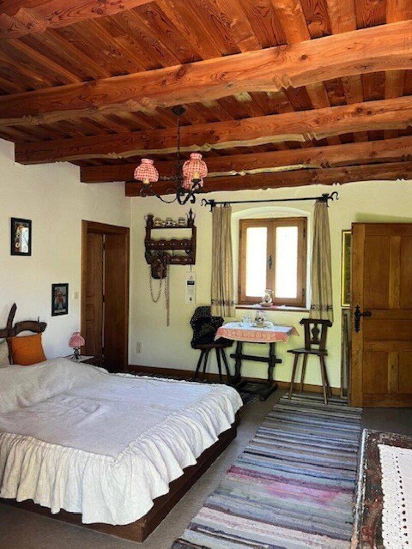 Schlafzimmer mit Holzbalkendecke, traditionellem Bett und Fenster mit Blick ins Grüne.