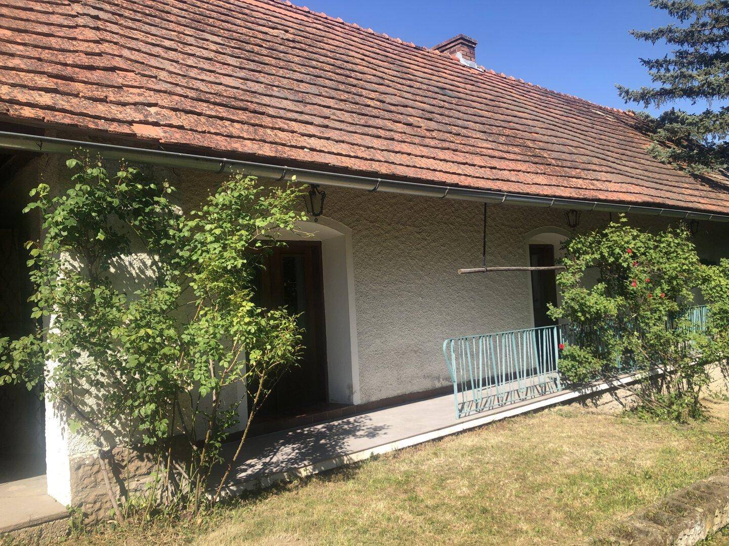 Seitenansicht des Hauses mit Ziegeldach, Regenrinne und einem kleinen Zugangsbereich.