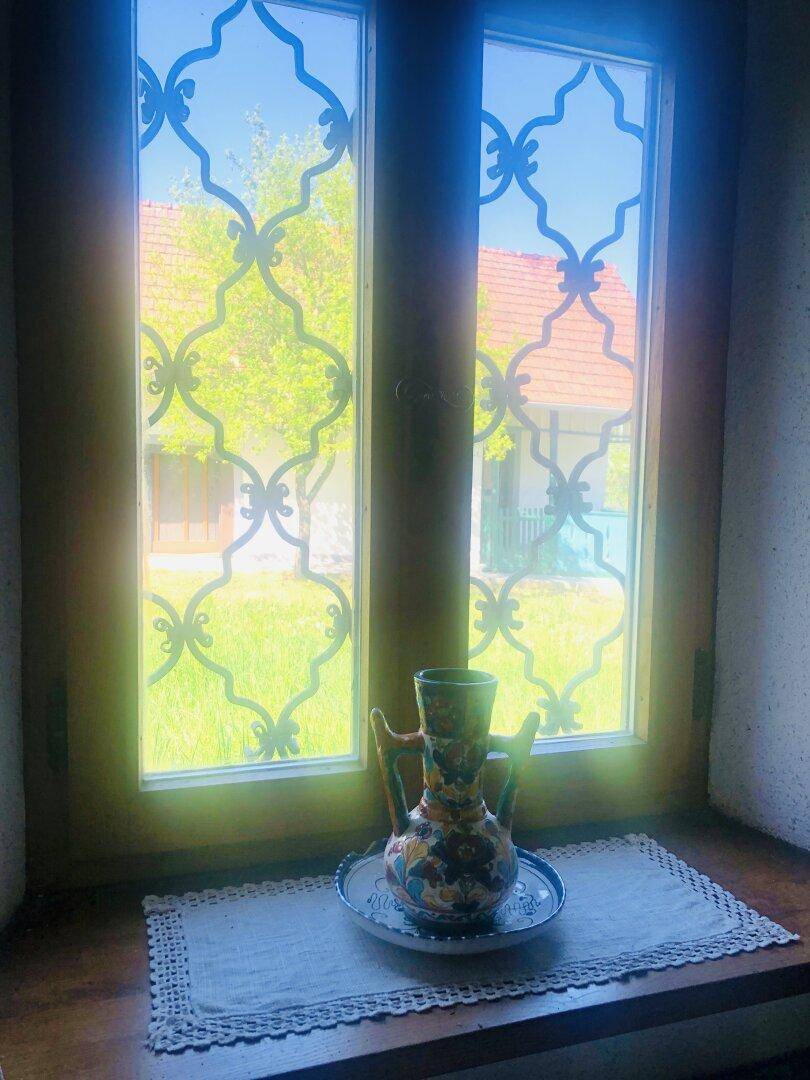 Fenster mit dekorativem Gitter und Blick auf den Garten, geschmückt mit einer Vase.