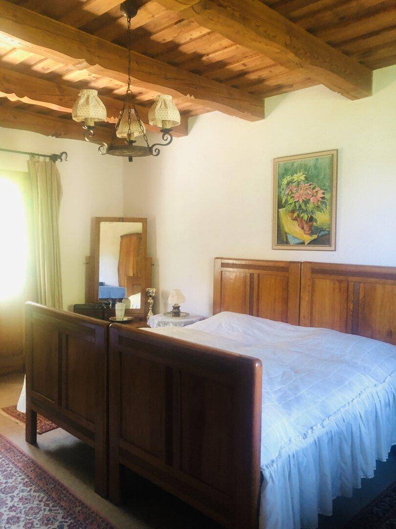 Helles Schlafzimmer mit Holzbalkendecke, traditionellem Bett und rustikalem Mobiliar.