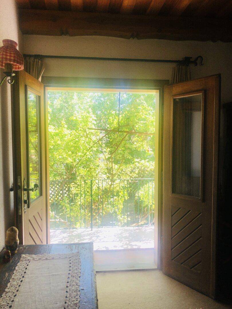 Offene Doppeltür führt von einem Innenraum auf einen Balkon mit Blick ins Grüne.