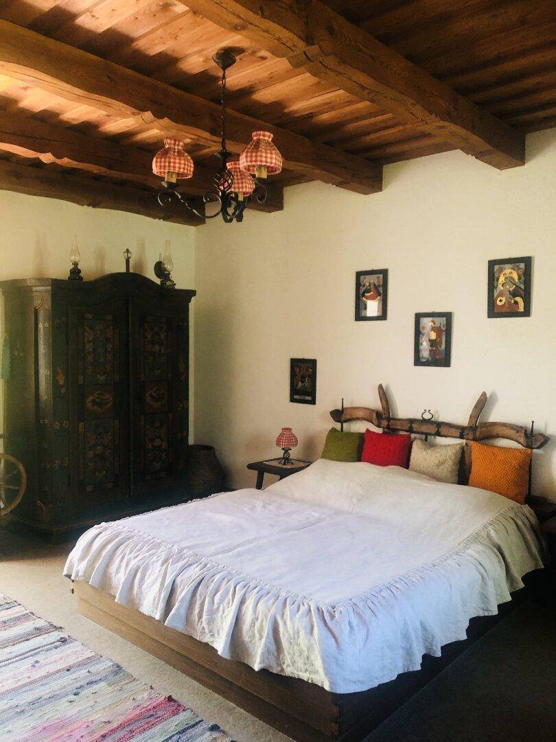 Geräumiges Schlafzimmer mit Holzbalkendecke, Kachelofen und traditionellen Möbeln.
