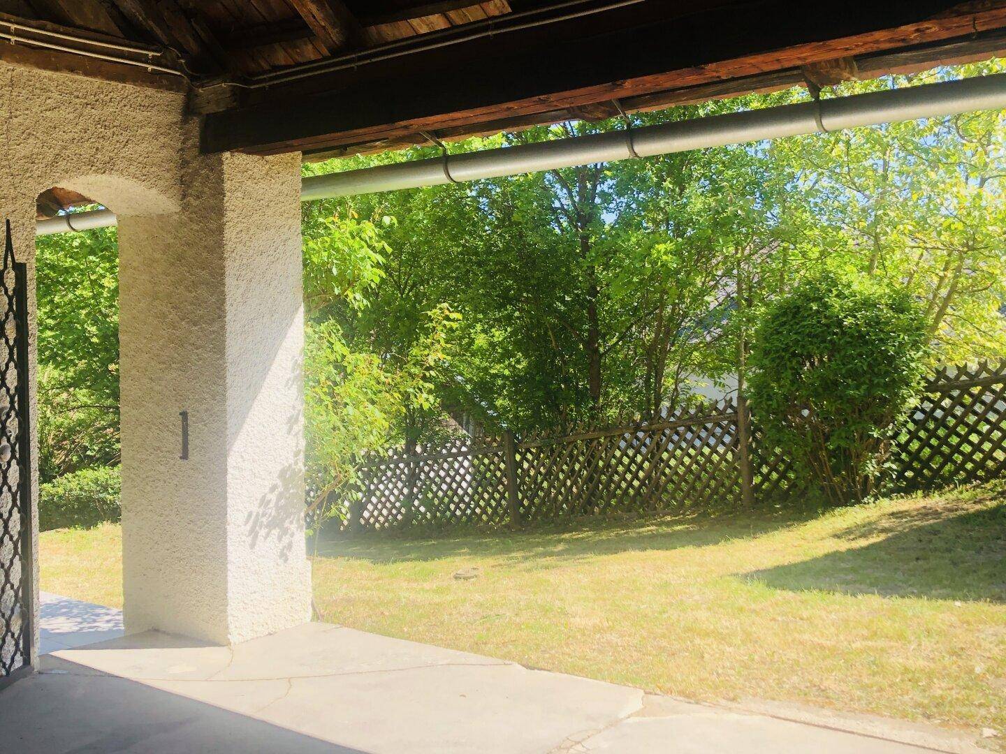 Überdachte Terrasse mit Blick auf den grünen Garten und einen dekorativen Holzzaun.