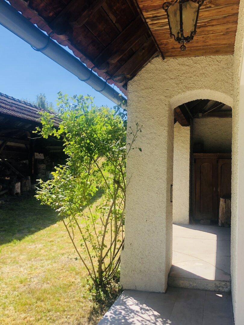 Überdachter Eingangsbereich oder Terrasse mit Blick auf den Garten und ein weiteres Gebäude.
