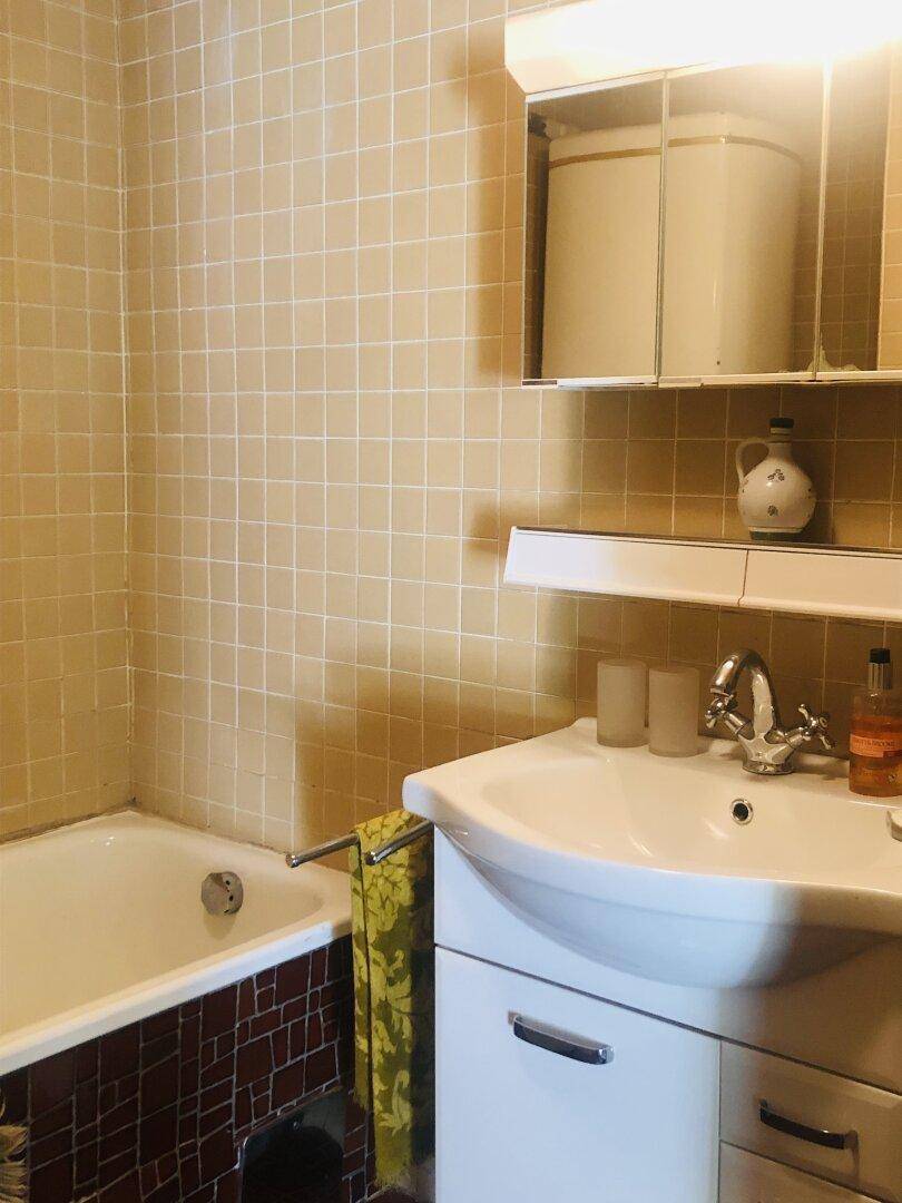 Badezimmer im 80er-Jahre-Stil mit beigefarbenen Fliesen, Badewanne und Waschbecken.