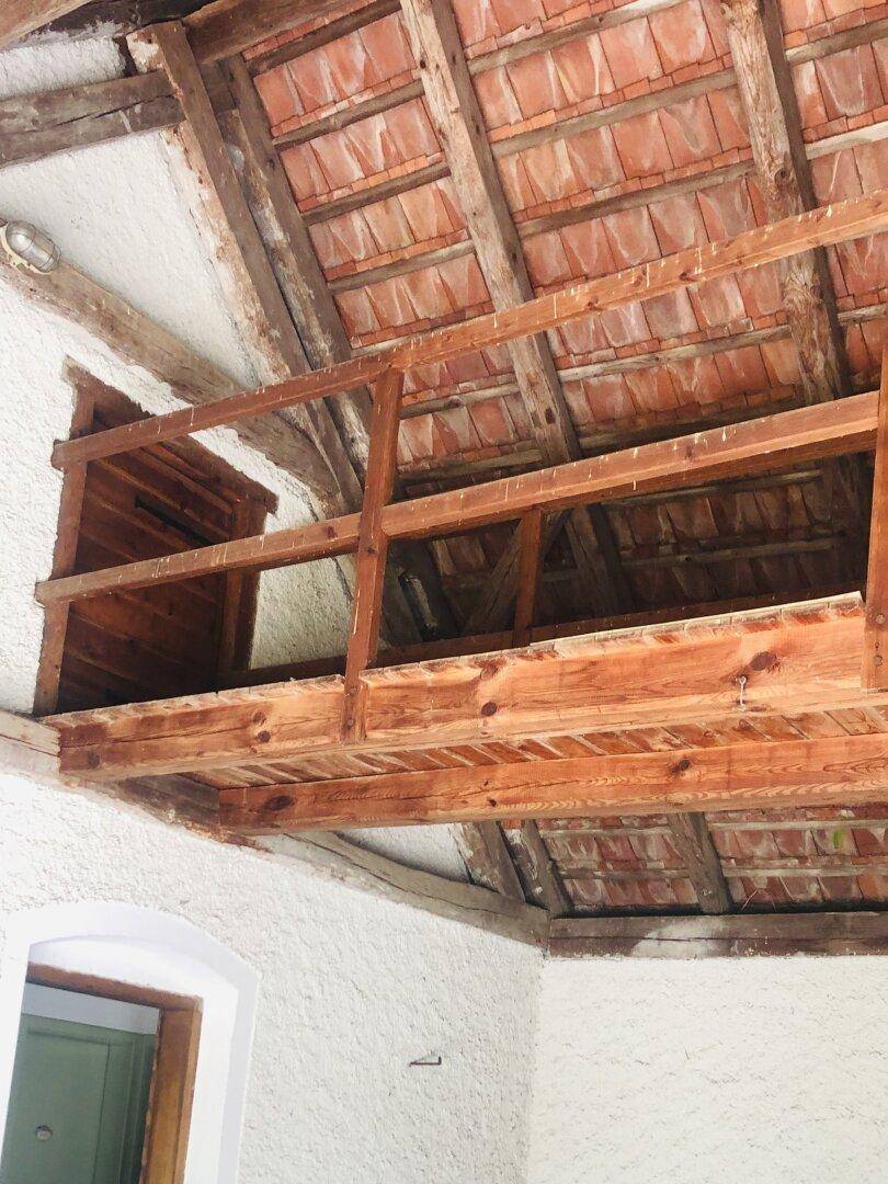 Detailansicht der rustikalen Holzbalkendecke und des Dachstuhls in einem überdachten Bereich.