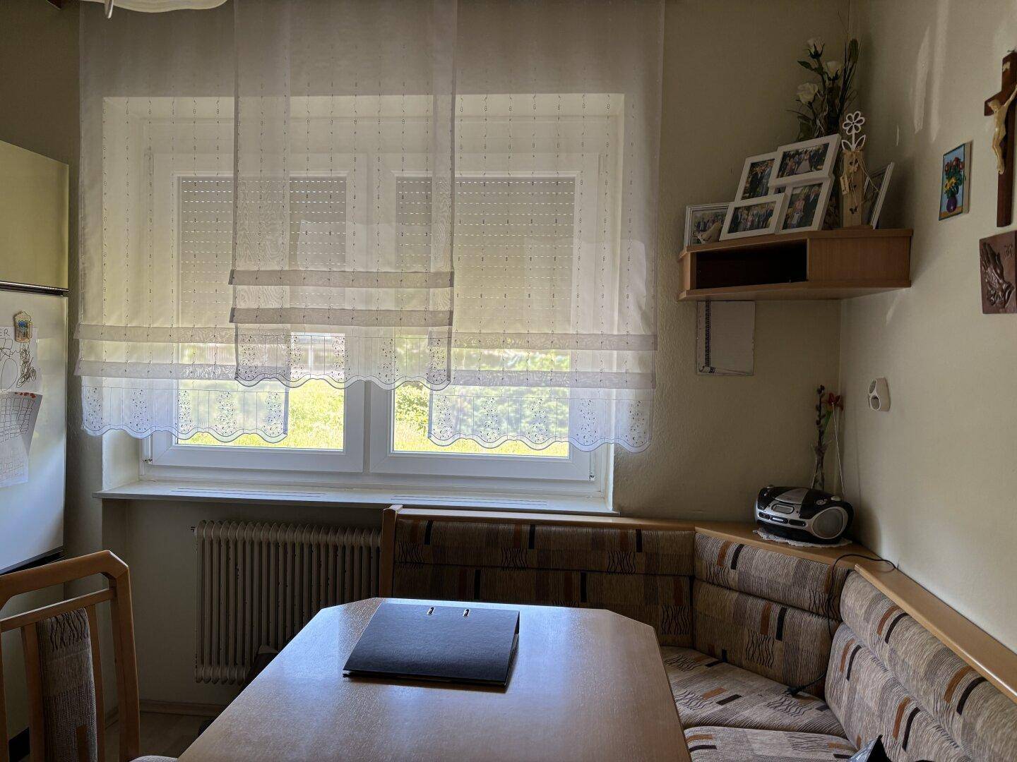 Essbereich in der Küche mit Eckbank, Esstisch und einem Fenster mit Spitzenvorhängen.