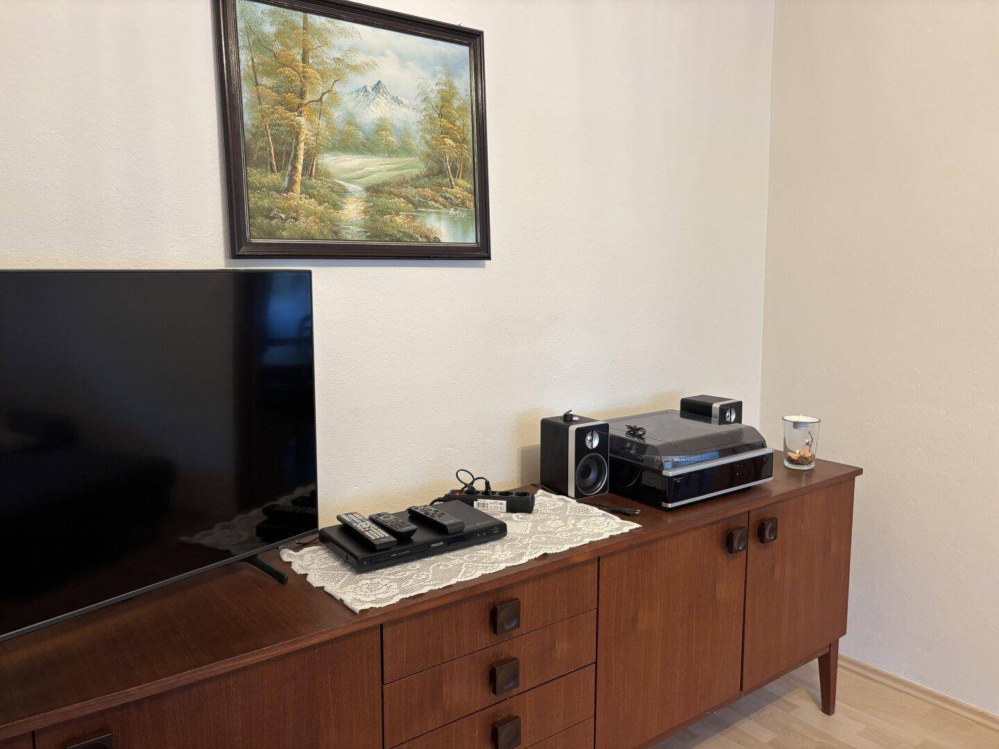 Detailansicht des Wohnzimmers mit einem Holzsideboard, Fernseher und Stereoanlage.