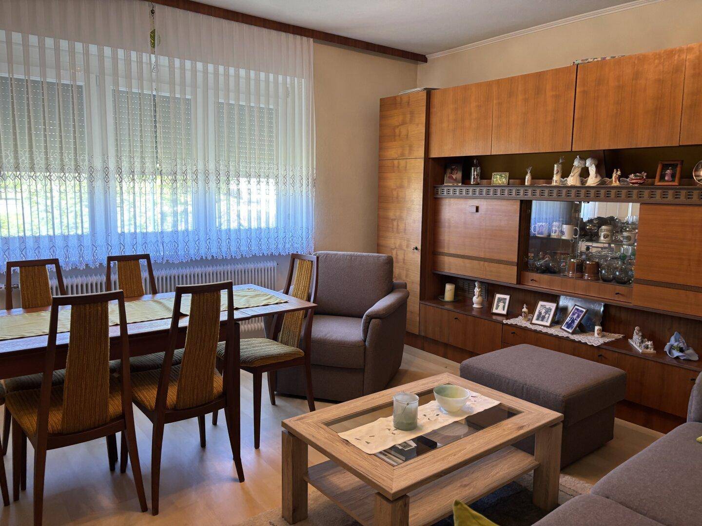 Wohn- und Essbereich mit Esstisch, Stühlen, Sofa und einer großen Holzschrankwand.