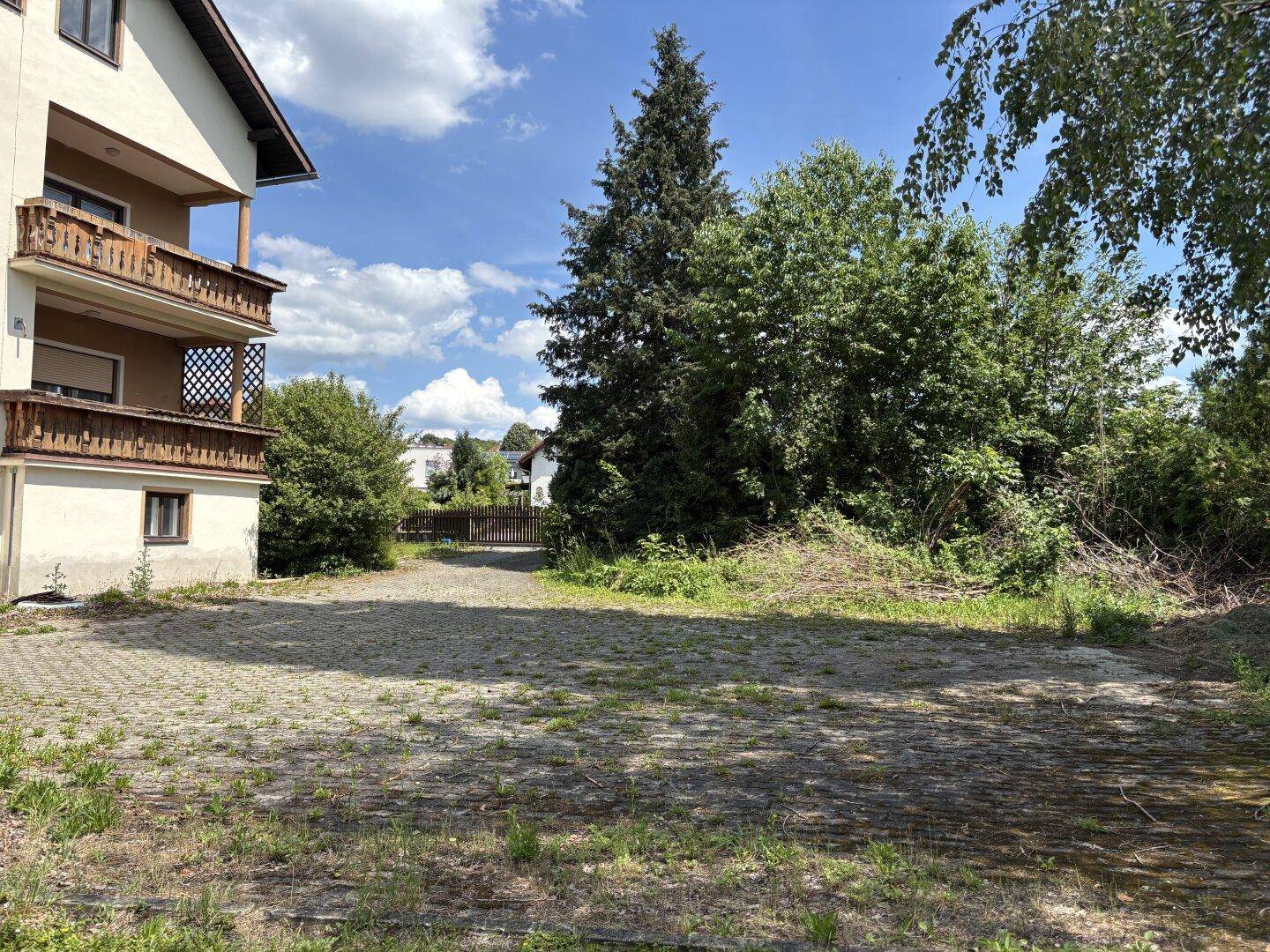 Große gepflasterte Fläche neben dem Haus, umgeben von Bäumen und Sträuchern.