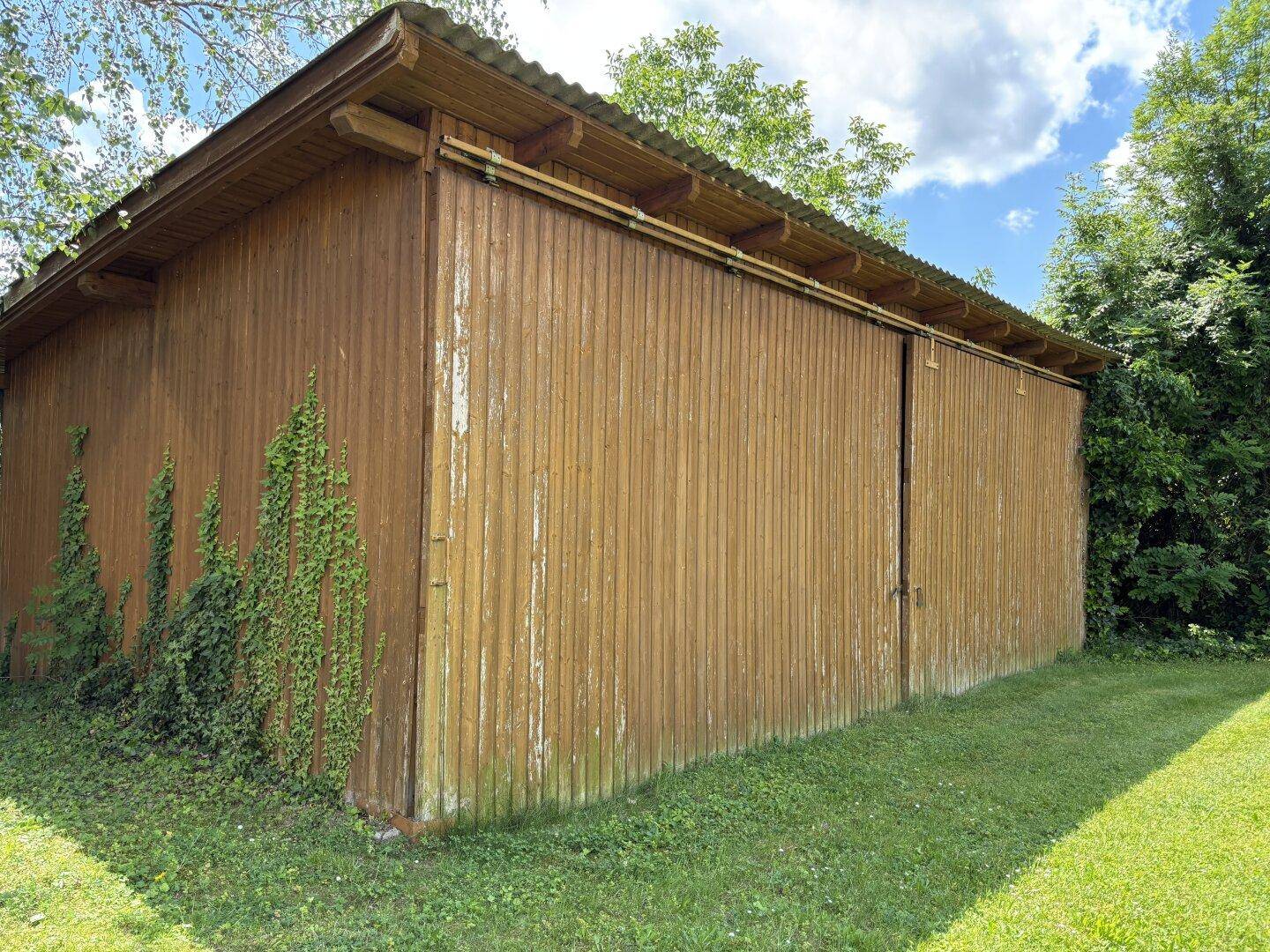 Rustikaler Holzschuppen im Garten mit leicht verwitterter Fassade und grüner Bepflanzung.