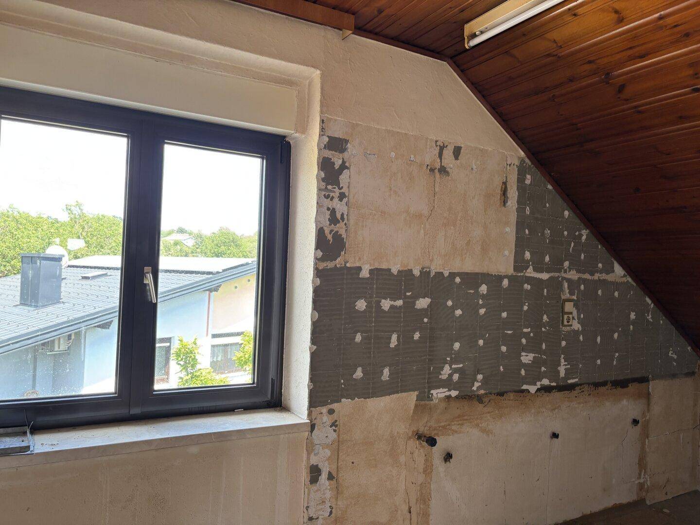 Dachgeschossraum im Rohbau mit Holzdachschrägen und einem Fenster mit Blick nach draußen.