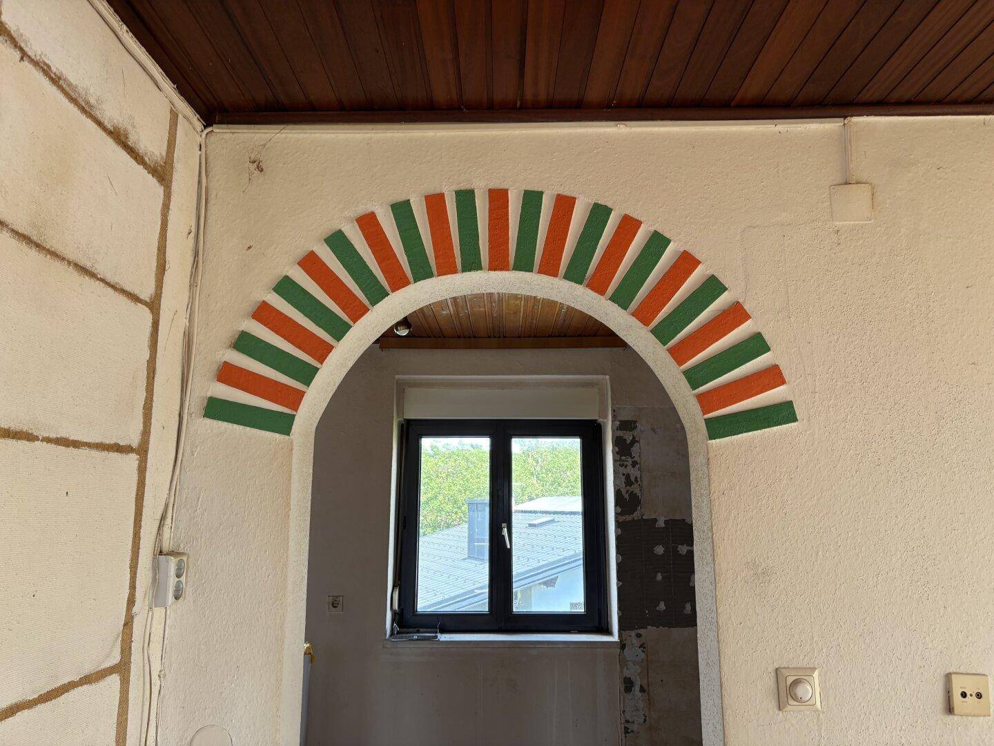 Innenraum mit einem dekorativen Bogen und einem Fenster, das Tageslicht spendet.