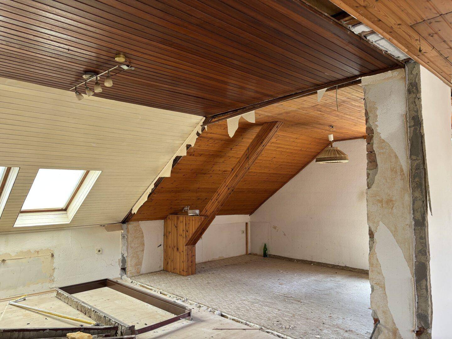 Dachgeschossraum im Rohbau mit Holzdachschrägen, Dachfenster und sichtbaren Balken.