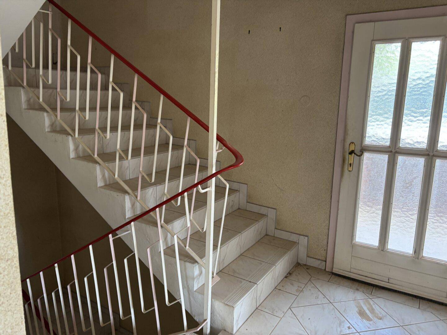 Treppenhaus mit gefliesten Stufen und einem roten Geländer, das in die obere Etage führt.