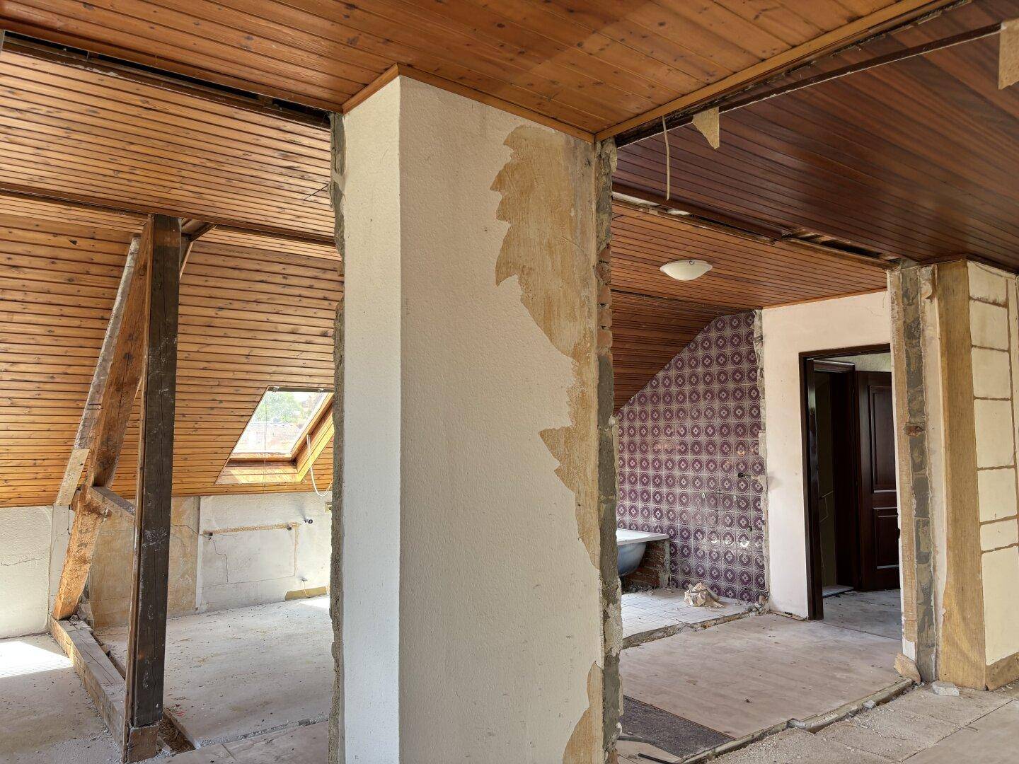 Innenraum im Umbau mit Holzbalken, Holzdecke und Blick in den zukünftigen Badbereich.