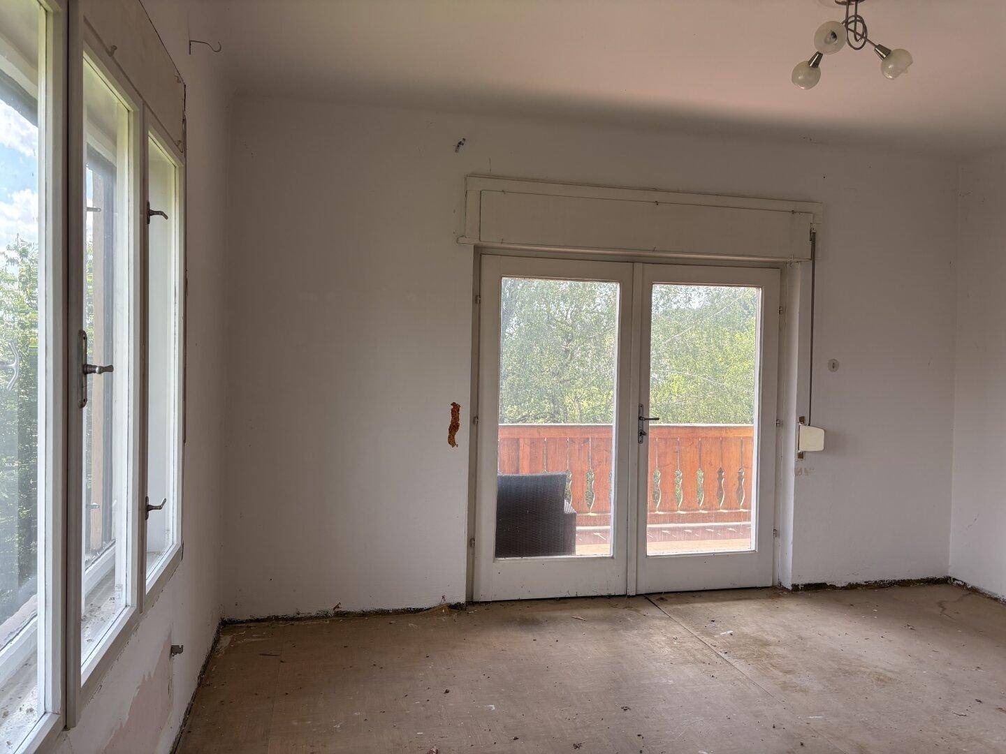 Leeres Zimmer mit Zugang zu einem Balkon und Fenstern, die viel Licht hereinlassen.