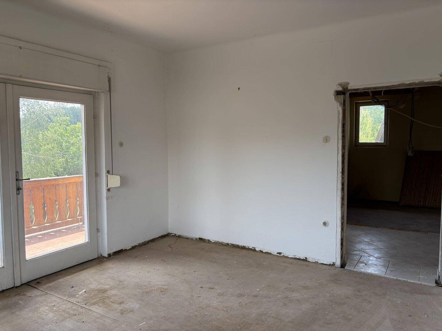 Unmöbliertes Zimmer mit weiß gestrichenen Wänden und Balkonzugang, bereit zur Renovierung.