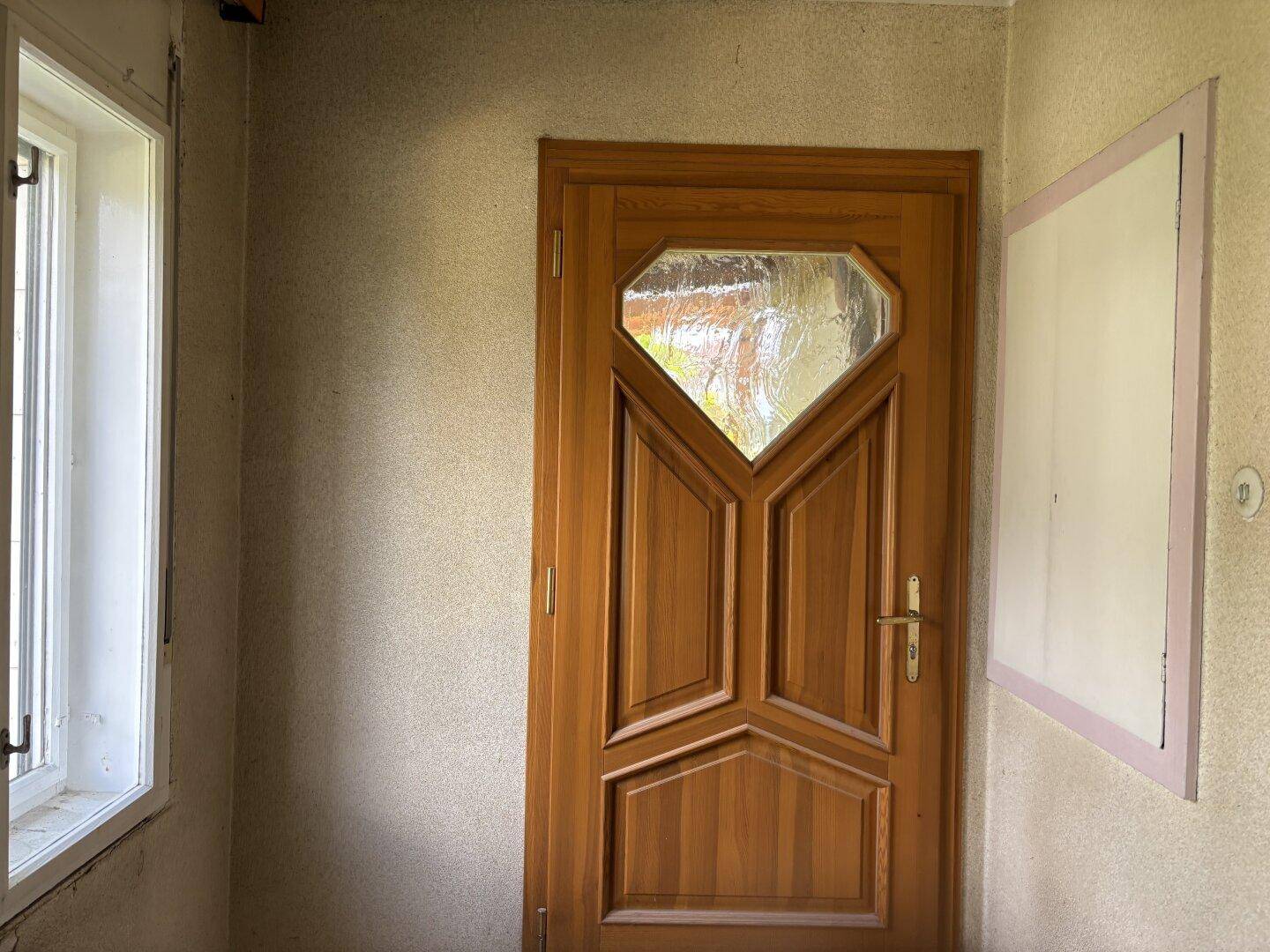 Eingangsbereich mit einer Holztür und einem Fenster, das Tageslicht hereinlässt.