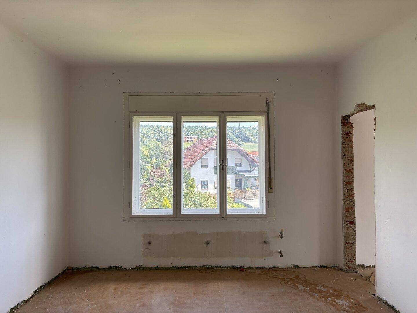 Unmöbliertes Zimmer mit weiß gestrichenen Wänden und einem Fenster mit Blick auf die Umgebung.