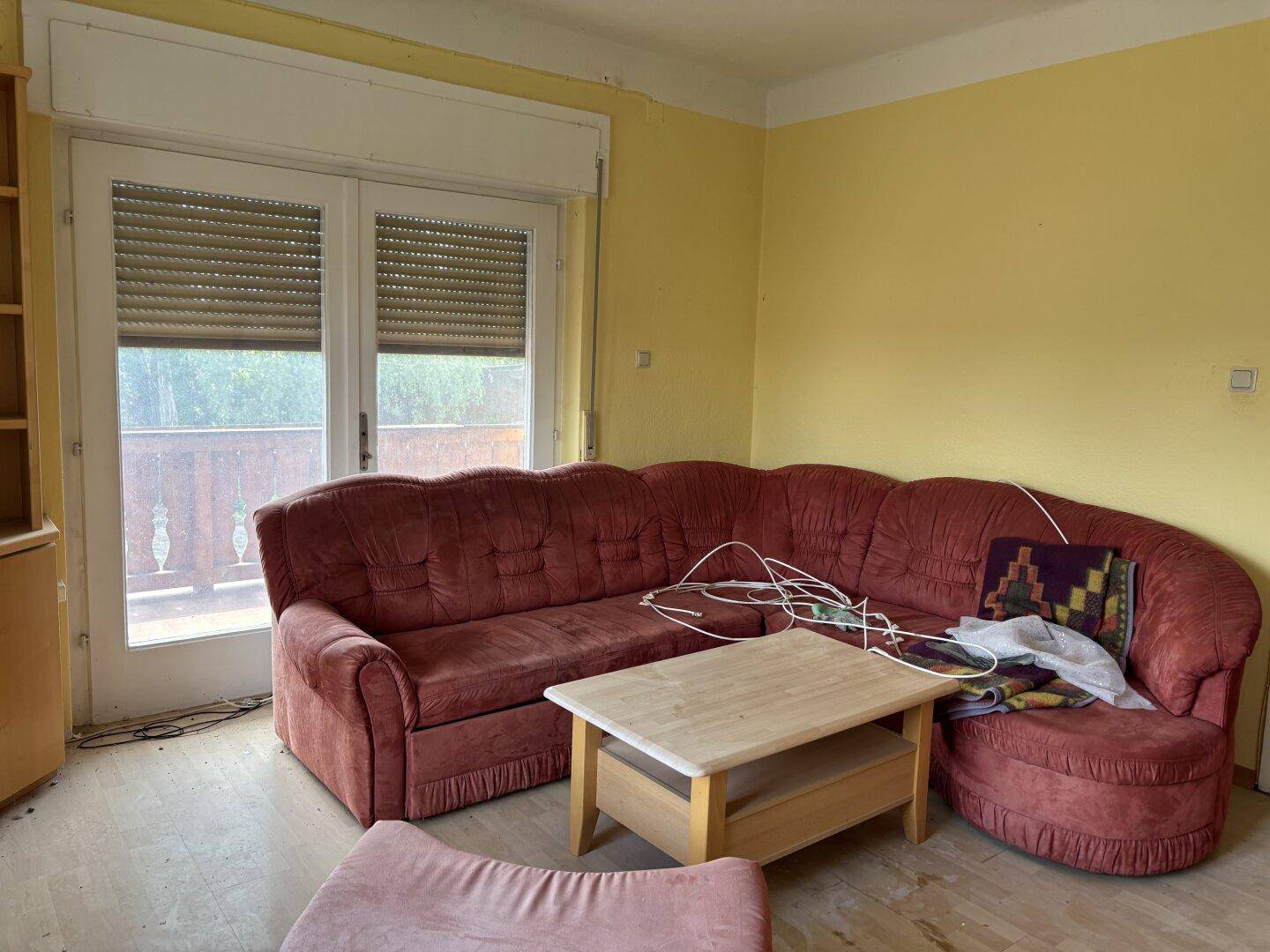 Wohnzimmer mit rotem Ecksofa, Couchtisch und Zugang zu einem Balkon.