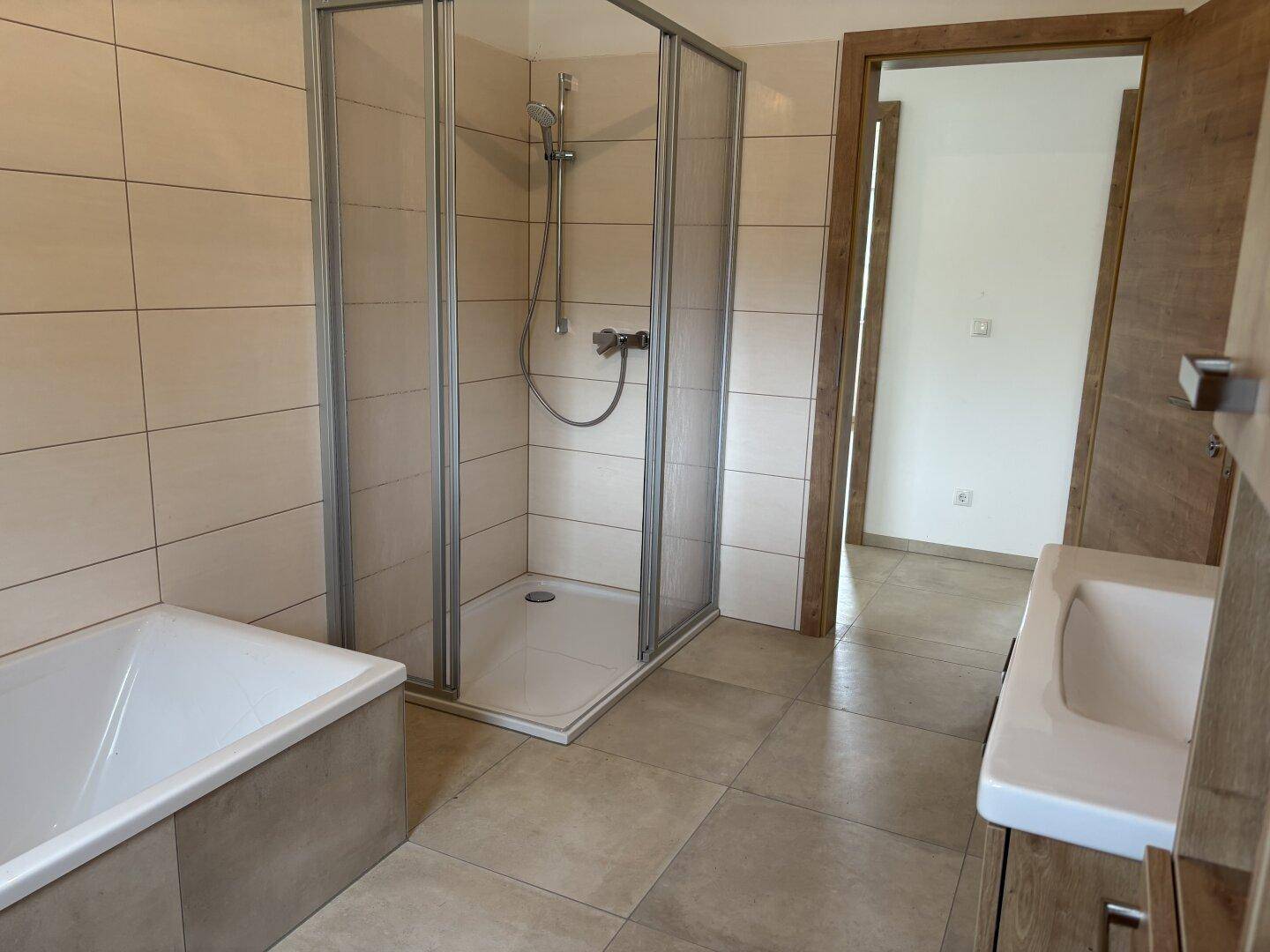 Modernes Badezimmer mit Duschkabine, Badewanne und Waschtisch in neuwertigem Zustand.