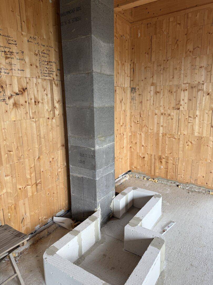Unfertiger Raum mit Holzwänden, Betonboden und einem gemauerten Kaminfundament.