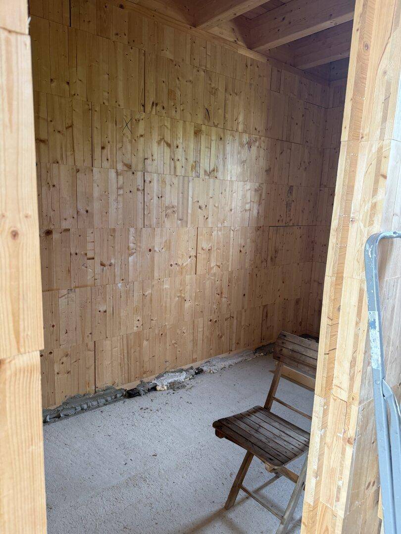 Einfacher, unfertiger Raum mit Holzwänden und Betonboden, bereit für den weiteren Ausbau.