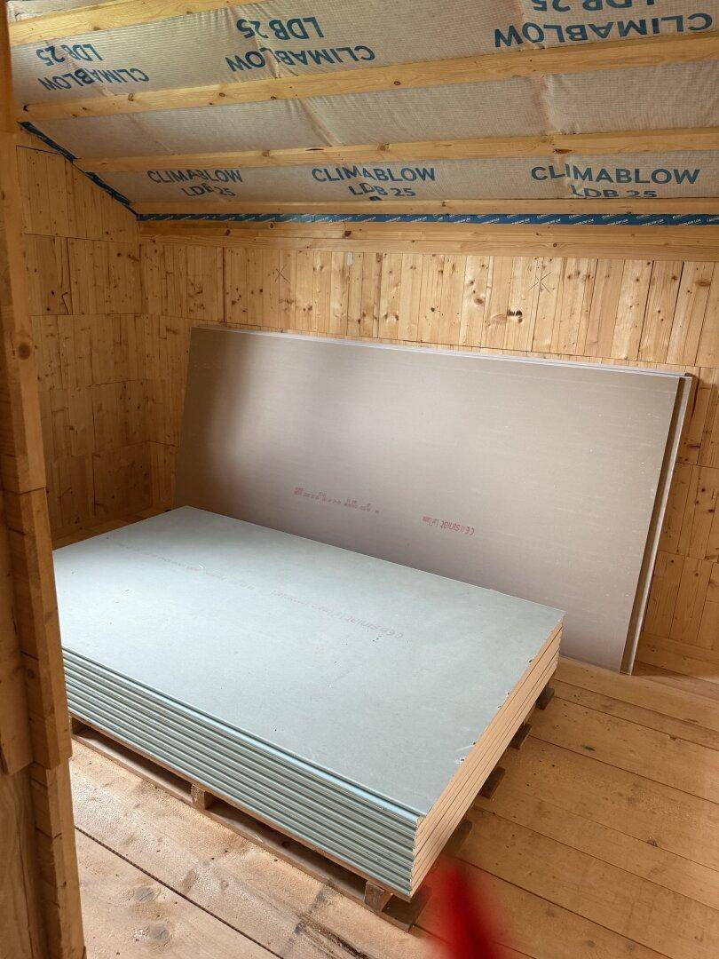 Dachgeschoss im Rohbau mit Holzwänden, Dachschräge und gestapelten Gipskartonplatten.