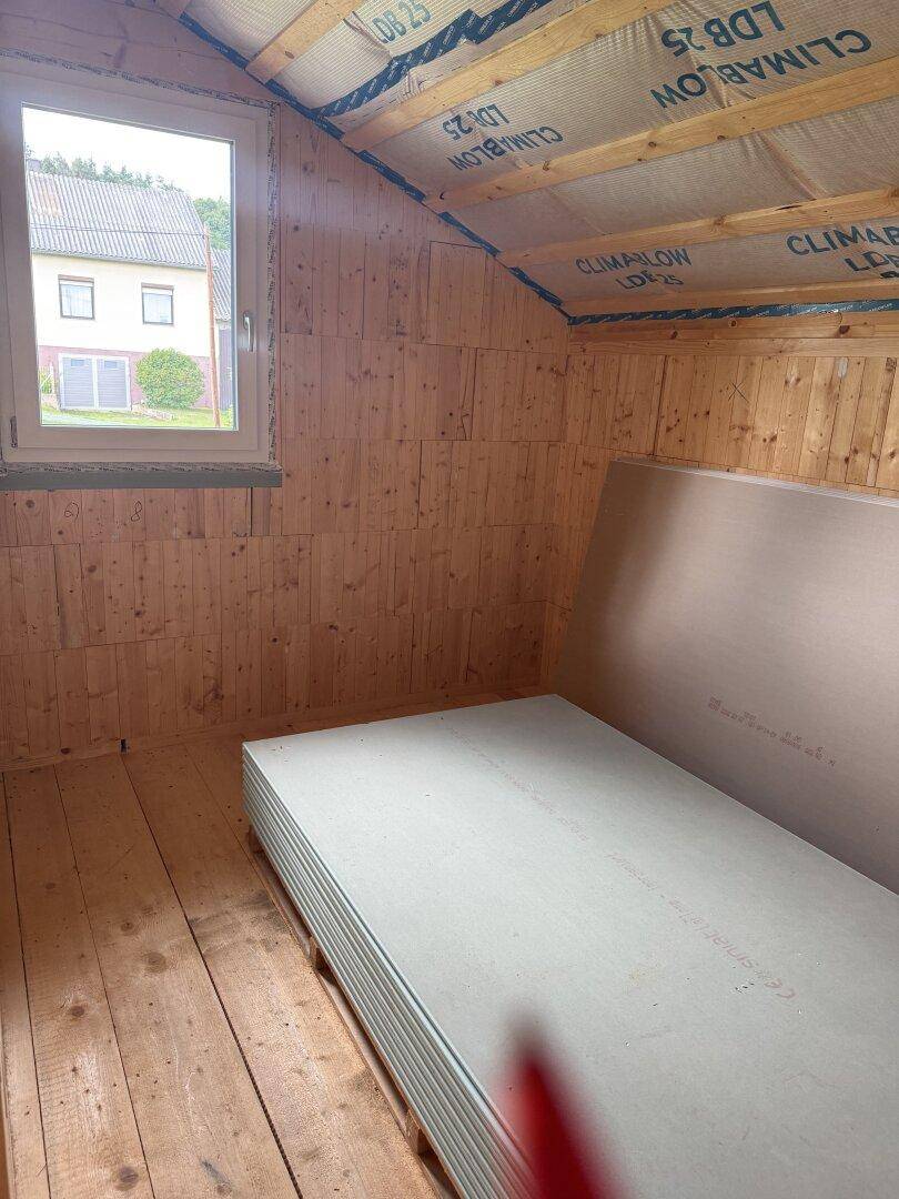 Helles Dachgeschoss mit Holzwänden, Dachschräge und Fenster, bereit für den Innenausbau.